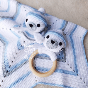 Manta de apego y sonajero con forma de foca invernal en colores blancos y azules, las cabezas de las foquitas están adornadas con gorros.