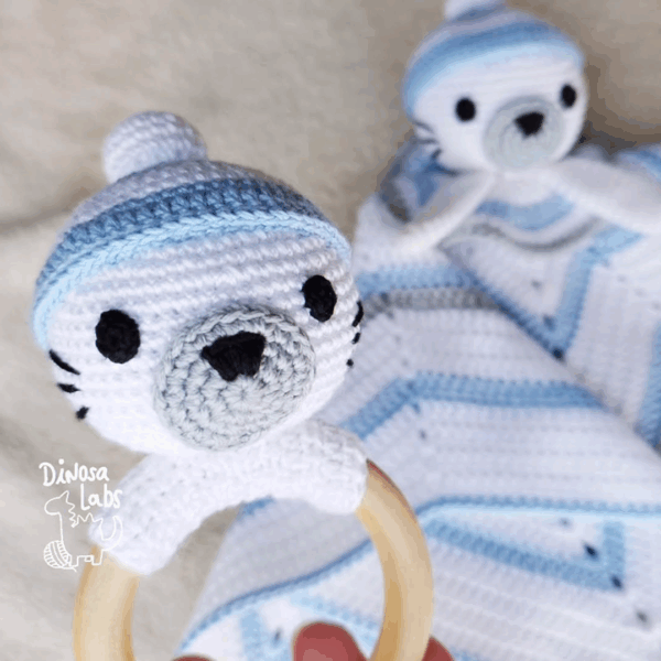 Manta de apego y sonajero con forma de foca invernal en colores blancos y azules, las cabezas de las foquitas están adornadas con gorros.